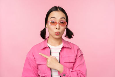 Portrait of young woman standing against pink background