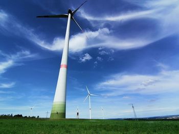 Low angle view of wind turbines on field against sky