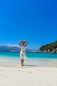 Full length of woman walking on beach against clear blue sky