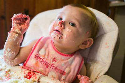 Cute baby girl with messy face sitting on chair at home