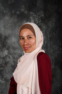 Portrait of smiling young woman standing against wall