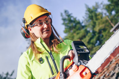 Female worker cutting tree trunk with electric saw