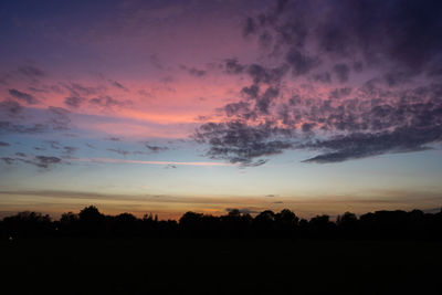 Silhouette trees on field against romantic sky at sunset