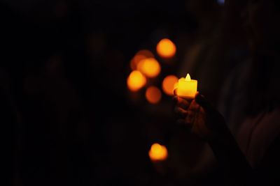 Close-up of hand holding illuminated candles against sky at night