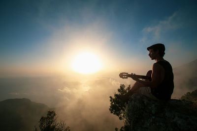 Man playing guitar on mountain during sunset