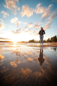 Full length of woman standing at beach against sky during sunset