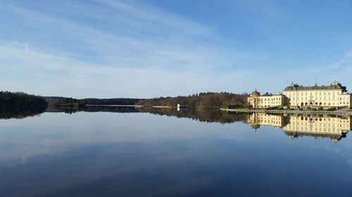 Reflection of drottningholm palace in river against sky on sunny day