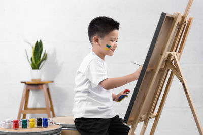 Side view of boy painting on canvas at home