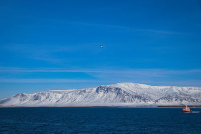 Scenic view of sea and snowcapped mountains against blue sky