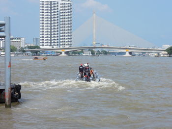 People on boat in sea against sky in city