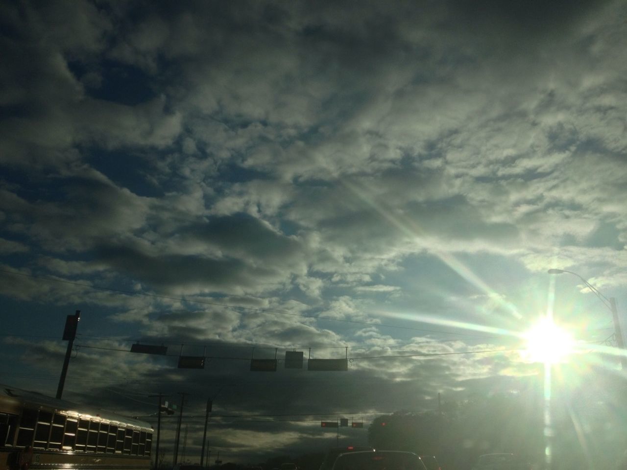 sky, cloud - sky, low angle view, built structure, sun, sunbeam, architecture, building exterior, street light, lens flare, cloudy, sunset, sunlight, silhouette, cloud, lighting equipment, outdoors, illuminated, weather, city