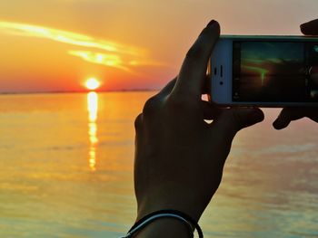 Man photographing sea against sky during sunset