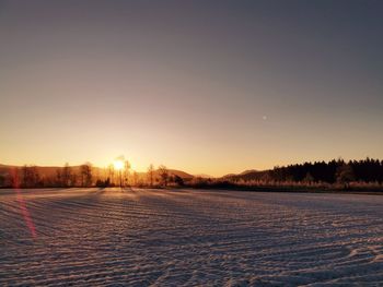 Snow covered field against sky during sunset