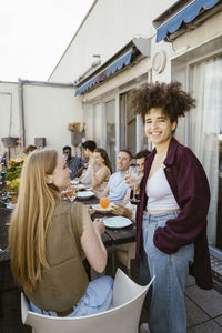 Smiling young woman enjoying food and drinks with friends at dinner party in balcony