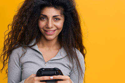 Portrait of young woman with camera against yellow background