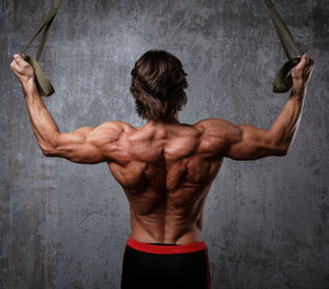 Shirtless muscular man exercising with arms raised standing against wall