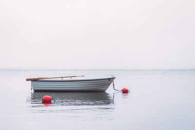 White boat with red buoys nearby in water against misty foggy sky