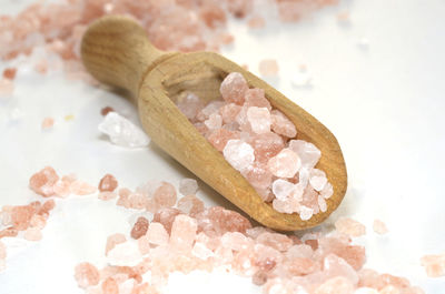 Close-up of rock salt with wooden spoon over white background