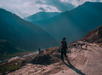 Rear view of man walking on mountain road against cloudy sky