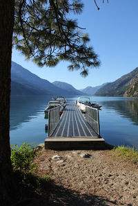 Boats moored near pier in lake by mountains against clear blue sky