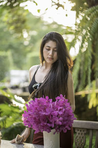 Beautiful woman standing by purple flowers in vase on table