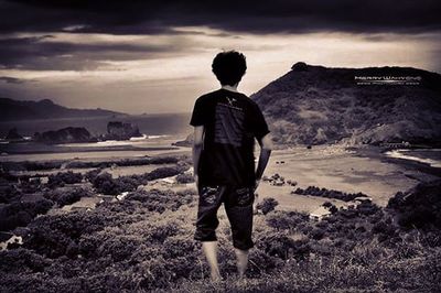 Rear view of woman standing on landscape against cloudy sky