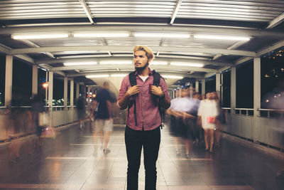 Young man looking away while standing on illuminated footbridge at night