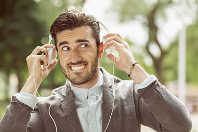 Happy businessman looking away while putting on headphones outdoors