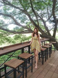 Full length portrait of smiling young woman against trees