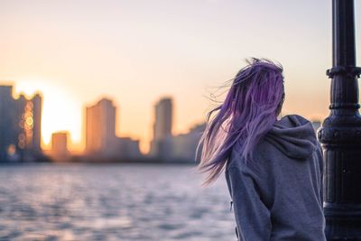 Rear view of young woman standing by sea against sky during sunset