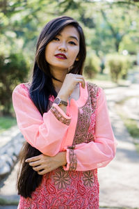 Portrait of beautiful young woman standing against pink background