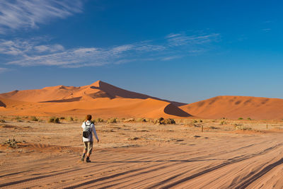 Rear view of hiker walking in namib desert against sky during sunny day
