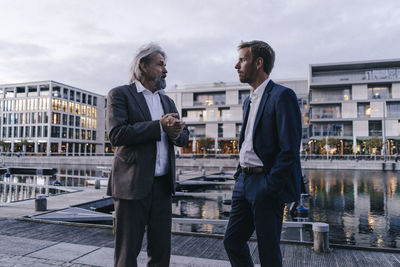 Two businessmen talking at city harbor at dusk