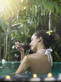 Woman taking bath with ladle in pool against trees