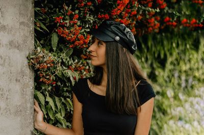 Woman in cap looking away against flowering plants