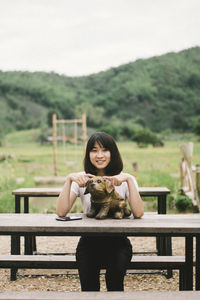 Portrait of smiling woman with dog statue sitting at picnic table 