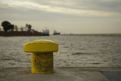 Close-up of yellow metal by sea against sky during sunset