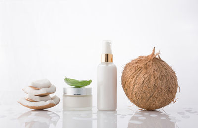 Stack of coconut pieces with beauty products against white background