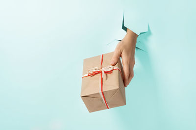 Close-up of female hand holding gift with ribbon through a torn blue paper. fast delivery creative