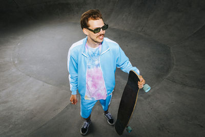 Smiling fashionable man in casuals standing with longboard on overpass road