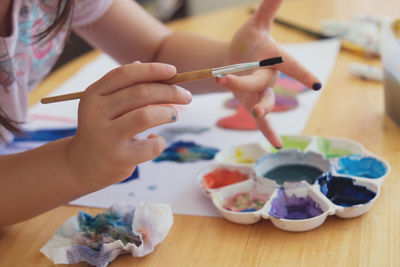 Cropped image of girl holding paintbrush at table