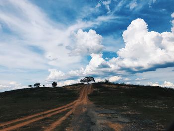 Empty road amidst field against sky