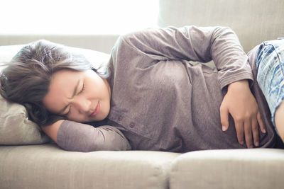Young woman suffering from stomachache while sleeping on sofa at home
