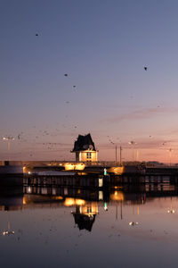 Birds flying over lake against sky during sunset