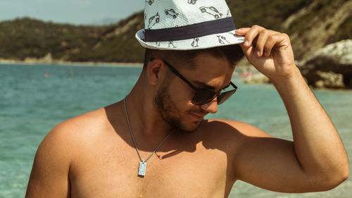 Shirtless young man wearing hat while standing against sea