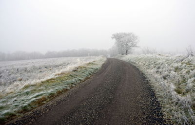 Road amidst field against sky during winter