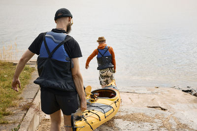 Rear view of men carrying kayak at coast