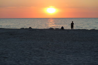 Silhouette people on beach against sky during sunset
