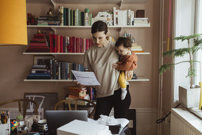 Female professional reading document while carrying son at home office