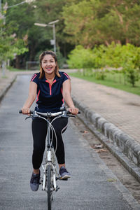 Portrait of smiling young woman riding bicycle on road
